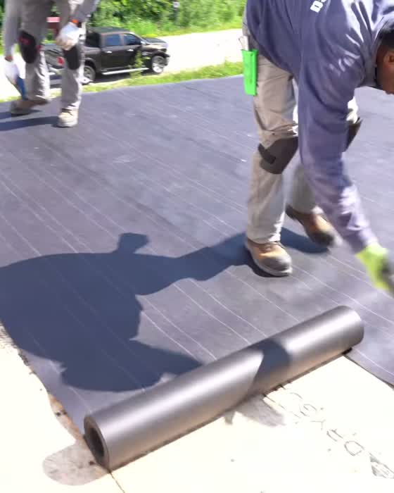 Roofer laying underlayment across a roof deck